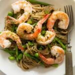 A bowl of sesame soba noodles with shrimp and a fork next to it.