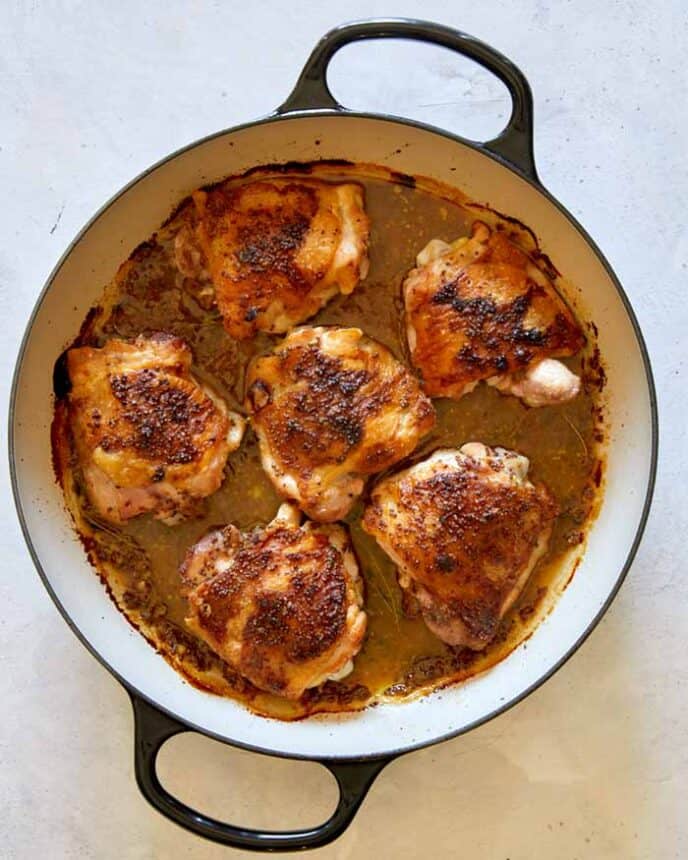 Baked chicken thighs with sauce in a skillet.
