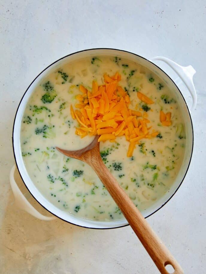 Hand fulls of cheese added into a stock pot to make broccoli cheddar soup.