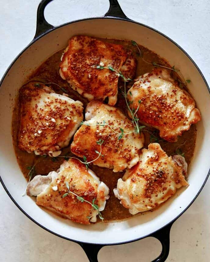 Seared chicken thighs with sauce poured over and sprigs of thyme.