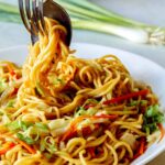 Chow mein noodles being picked up by a fork and spoon.