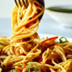 Close up on chow Mein Noodles being picked up with a fork and spoon.