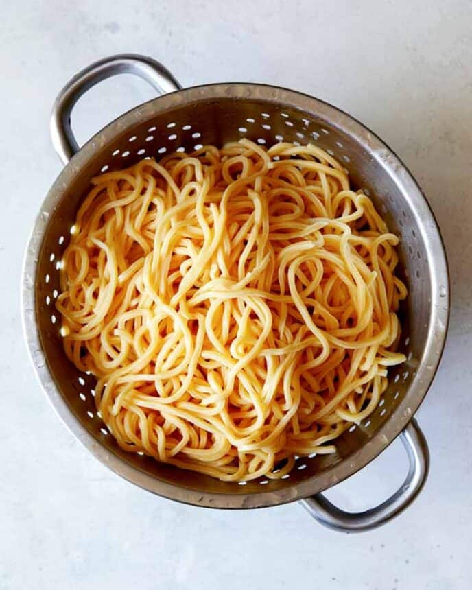 Cooked Chinese style egg noodles sitting in a colander.