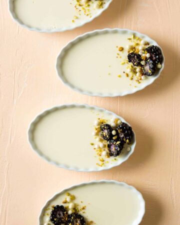 Four ramekins of creme fraiche panna cotta on a peach surface.