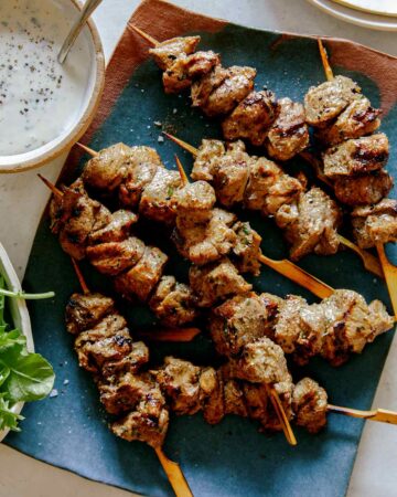 Lamb kabobs on a platter skewered with a side of yogurt sauce.