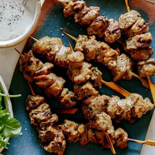 Lamb kabobs on a platter skewered with a side of yogurt sauce.