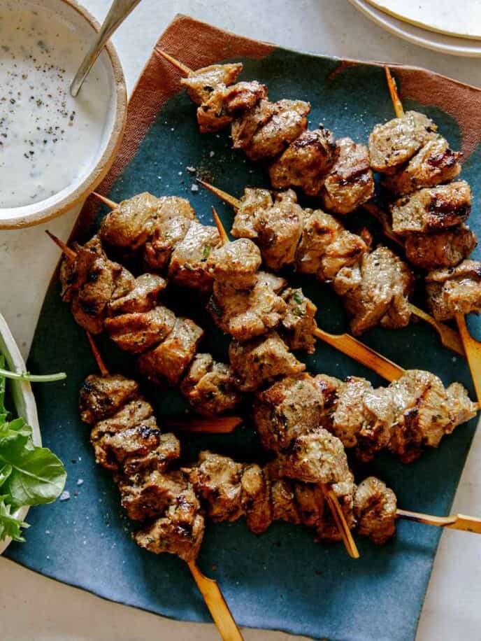 Lamb kabobs on a platter skewered with a side of yogurt sauce. 