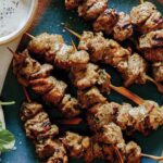 Lamb kabobs on a platter with a mint yogurt sauce next to it.