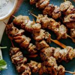 A platter of lamb kabobs with a salad next to it.