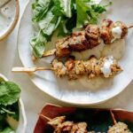 A serving of lamb kabobs on a plater with a mint yogurt sauce.