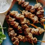 Lamb kabobs on a platter with a mint yogurt sauce next to it.