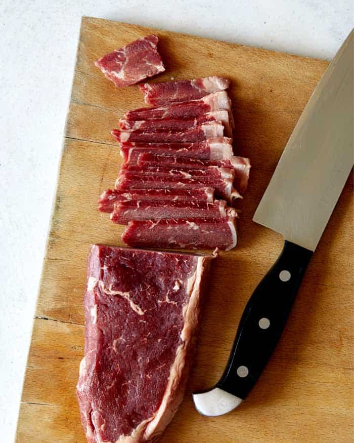 Slicing strip steak on a cutting board for Mongolian Beef.