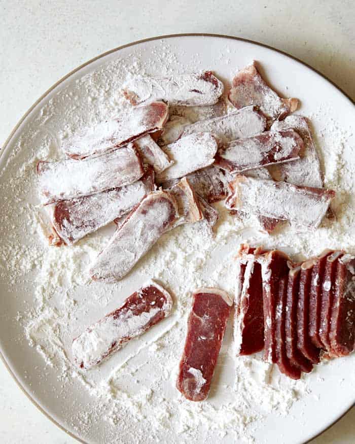 Tossing seasoned strip steak in cornstarch to make Mongolian Beef.