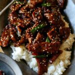 Mongolian Beef on a platter with bowls next to it.