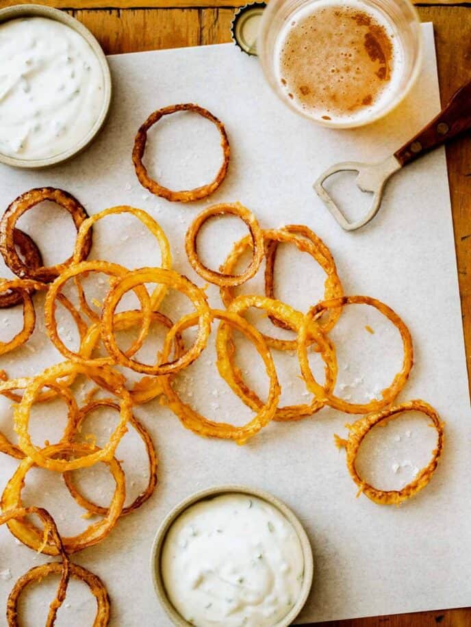 Homemade onion rings on a parchment with aioli and some glasses of beer.