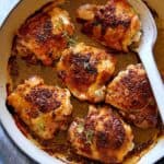 Oven baked chicken thighs in a skillet with a serving spoon.