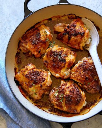 Oven baked chicken thighs with a spoon to serve.