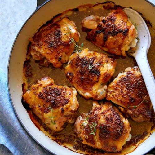 Oven baked chicken thighs with a spoon to serve.