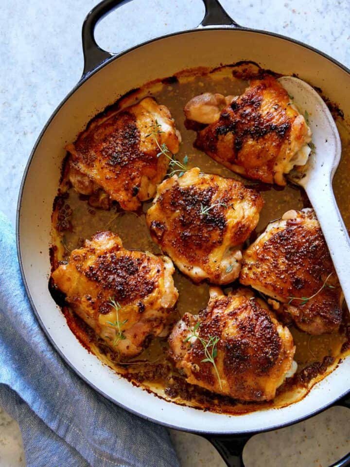 Oven baked chicken thighs with a spoon to serve.