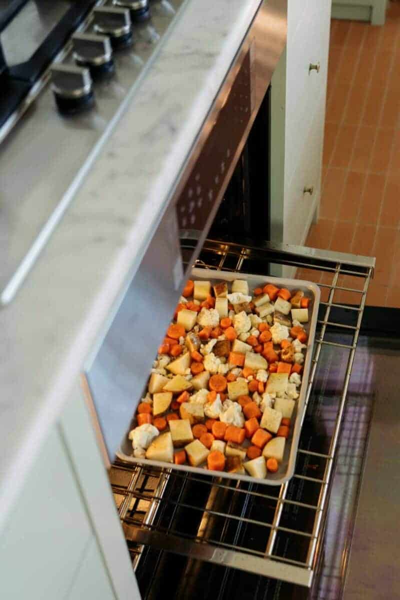 A sheet pan of vegetables going into an oven to be roasted.
