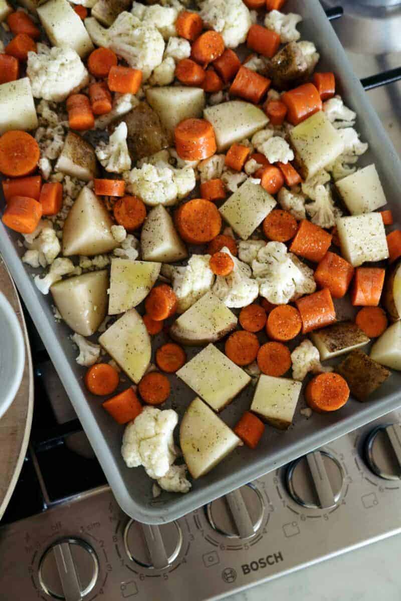 A sheet pan full of seasoned vegetables on top of an oven.