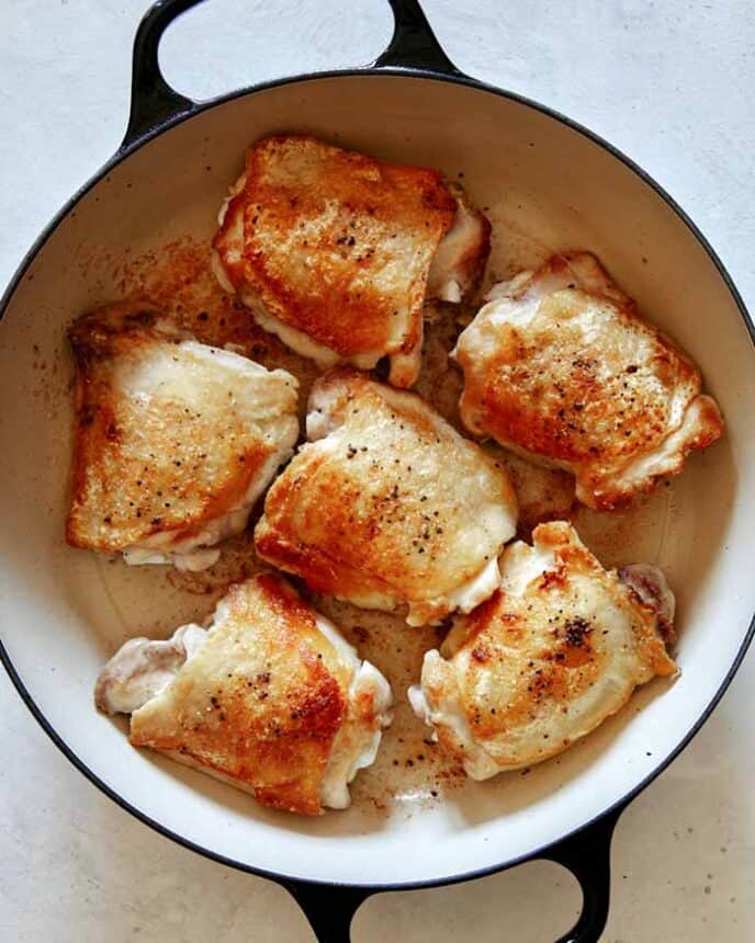 Seared and seasoned chicken thighs in a skillet.