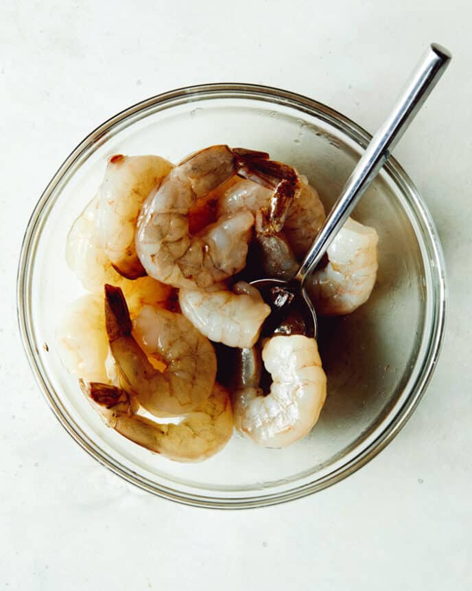 Uncooked shrimp in a glass bowl with fish sauce and oil.