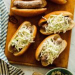 Mustard topped slaw bratwursts on a cutting board.