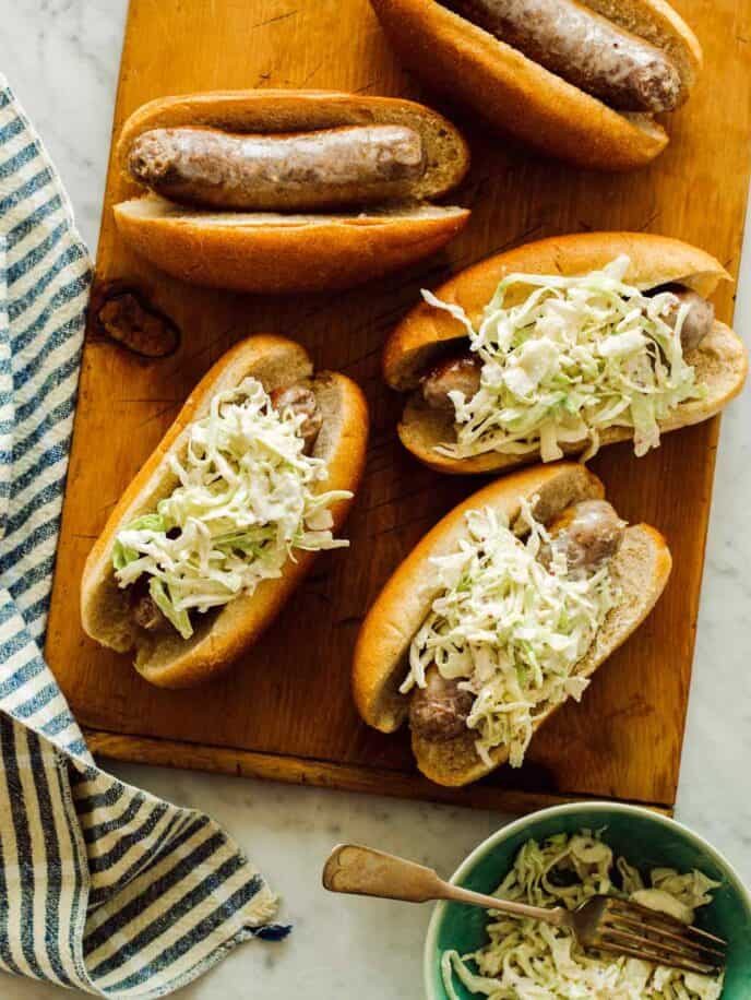 Mustard topped slaw bratwursts on a cutting board. 