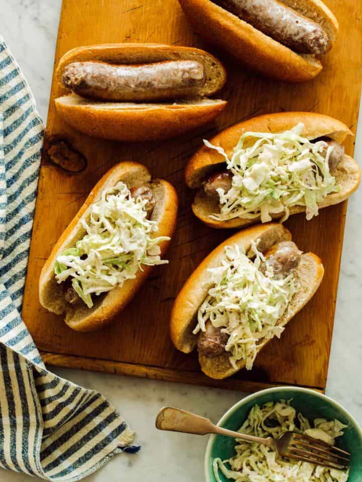 Mustard topped slaw bratwursts on a cutting board.