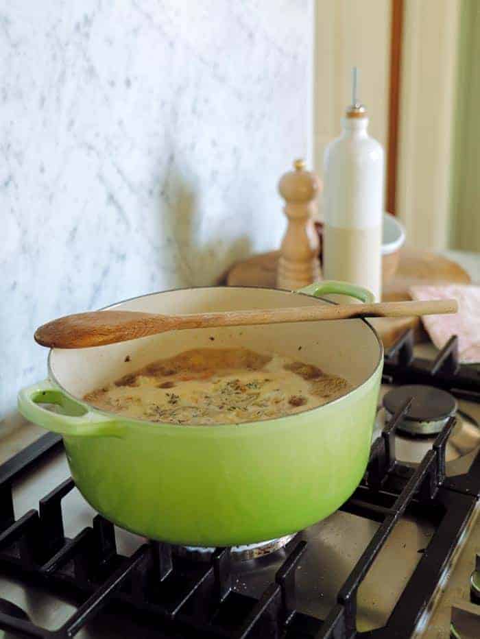 A green pot of soup simmering on a stovetop with a wooden spoon.