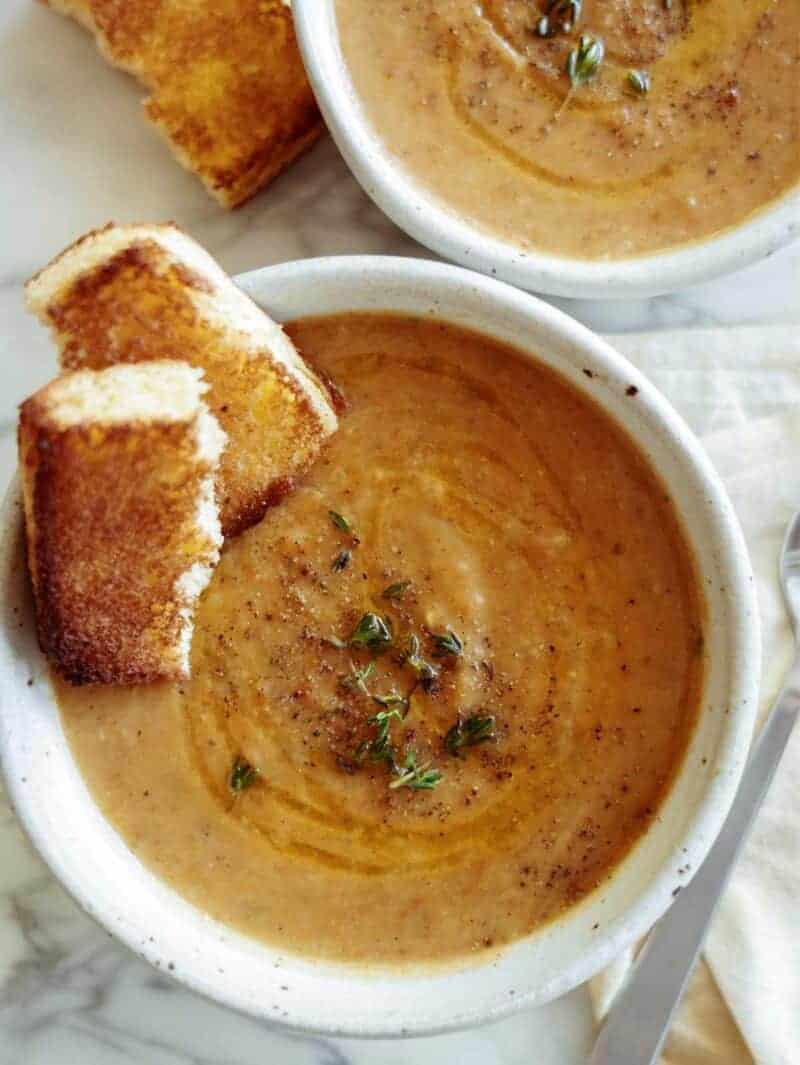 Two bowls of leftover vegetable soup with bread on the side. 