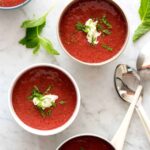 Four bowls of strawberry gazpacho with mint on the side.