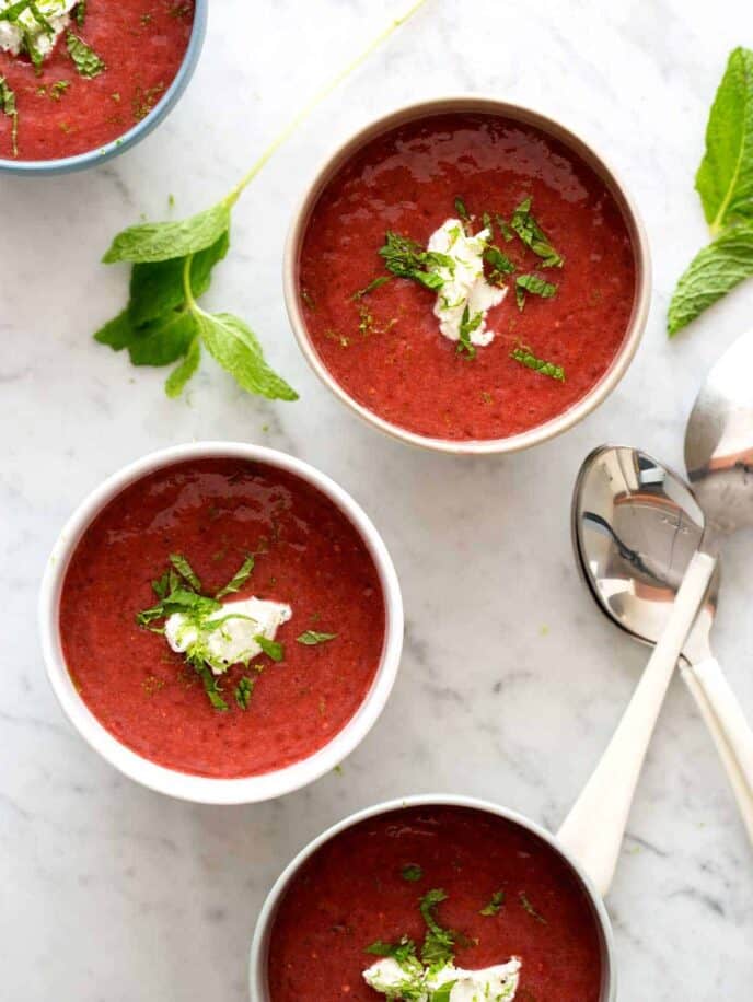 Four bowls of strawberry gazpacho with mint on the side.