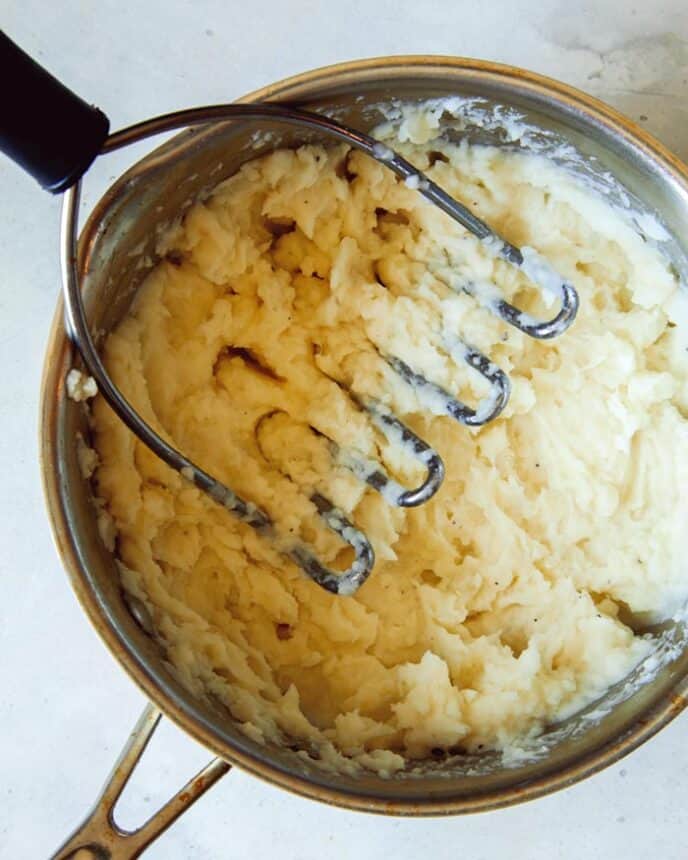 Combining potatoes with a potato masher. 