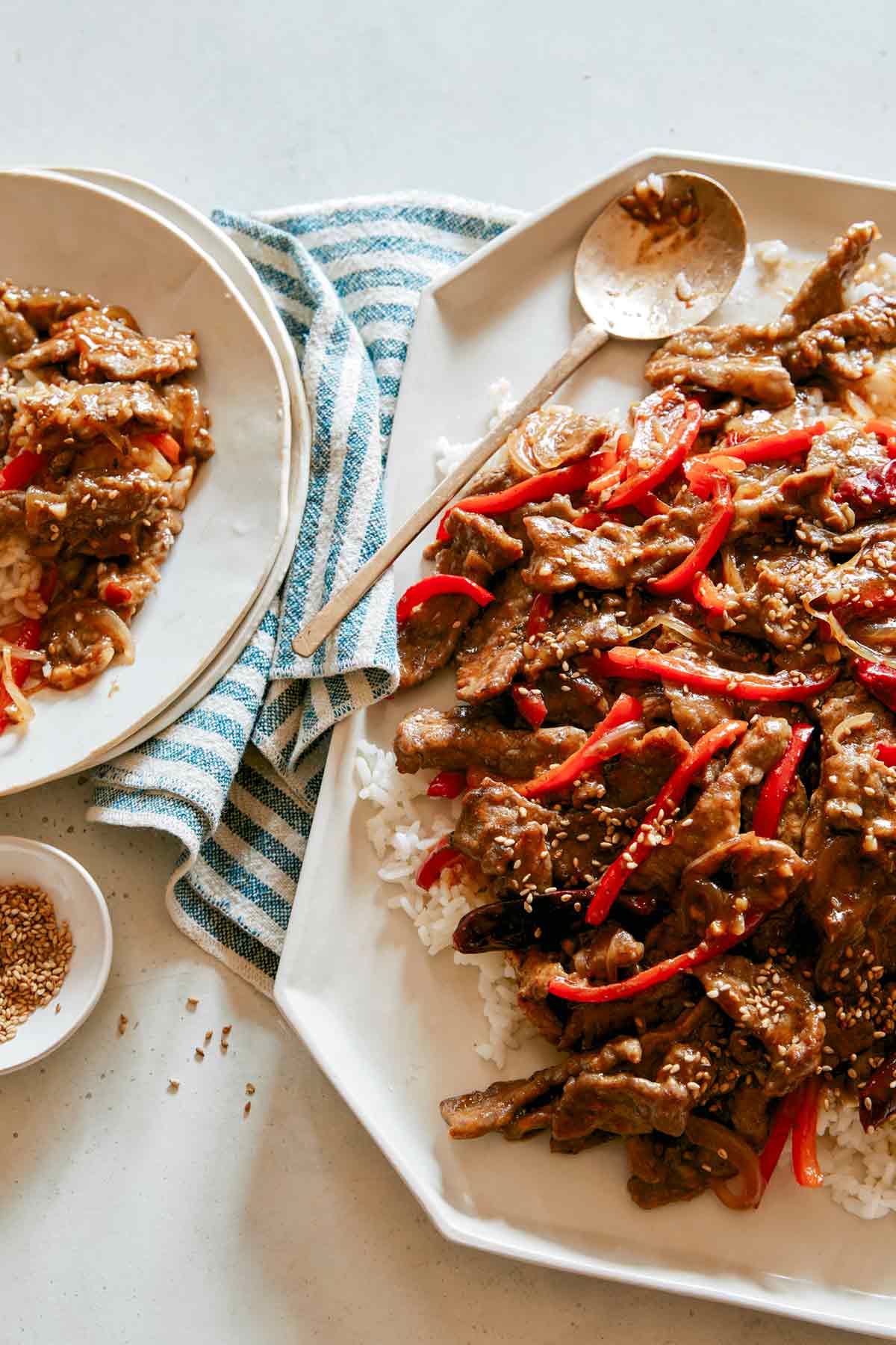 Szechuan beef on a platter with some served on a plate next to it. 