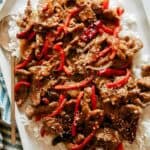 Close up on a platter of Szechuan beef over rice with a spoon on the side.