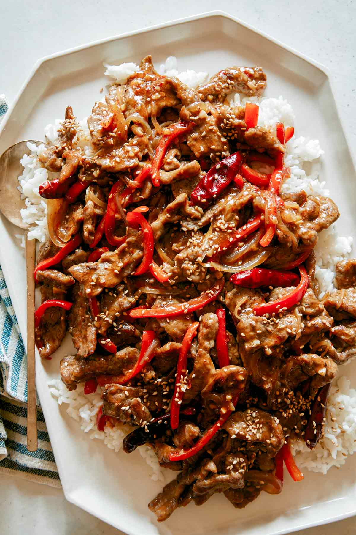 Szechuan Beef over rice on a platter with a spoon in it.