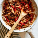 Szechuan Beef recipe in a skillet with a spoon in it.