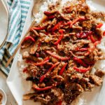 Szechuan Beef on a platter with a ramekin of sesame seeds next to it.