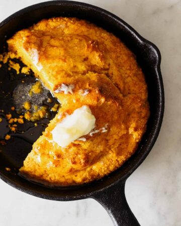 Pumpkin Cornbread in a skillet with butter on top.