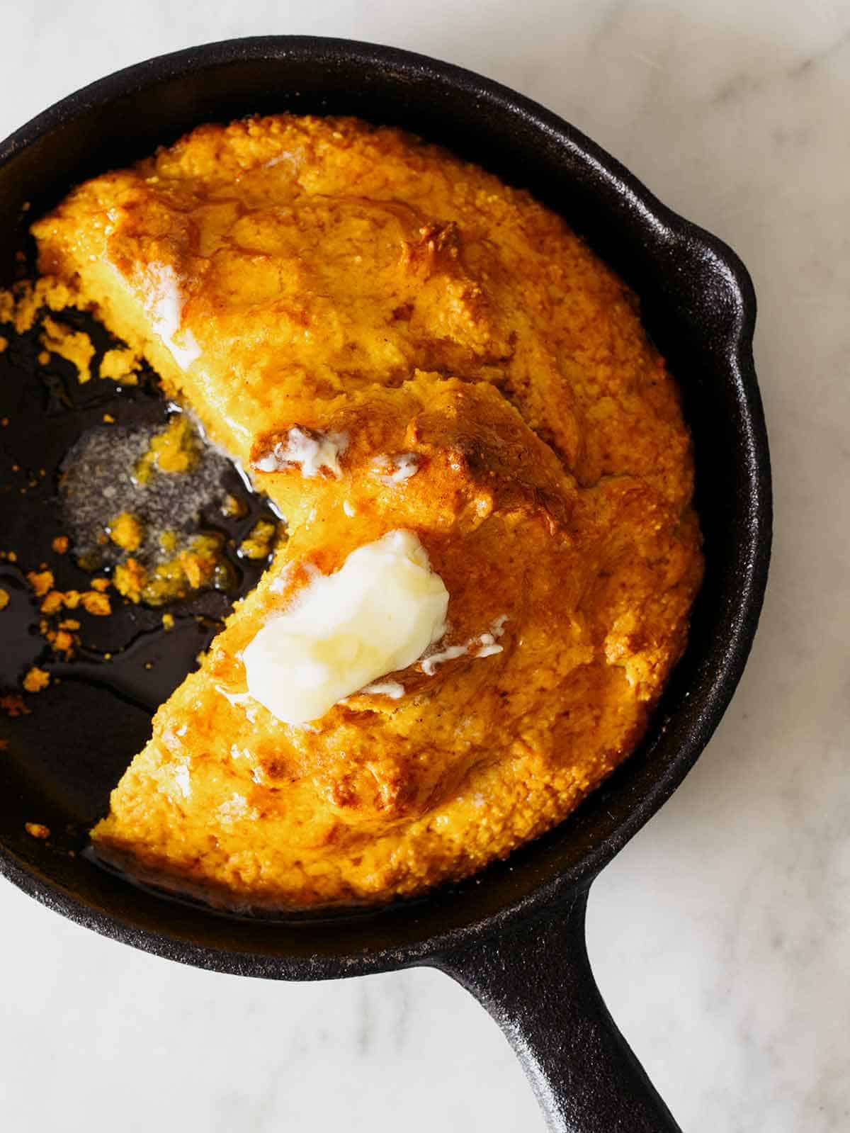 Pumpkin Cornbread in a skillet with butter on top. 