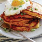 Cheesy Pumpkin Pancakes on a plate with a plate in the background of more pancakes.