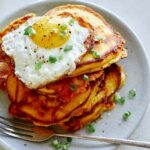 Cheesy Pumpkin Pancakes on a plate with a plate in the background of more pancakes.