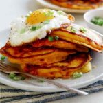 Cheesy Pumpkin Pancakes on a plate with a plate in the background of more pancakes.