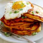 Cheesy Pumpkin Pancakes on a plate with a plate in the background of more pancakes.