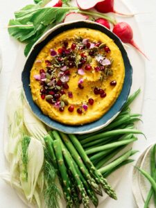 Roasted pumpkin hummus in a bowl with vegetables on the side, part of our Thanksgiving appetizers collection.