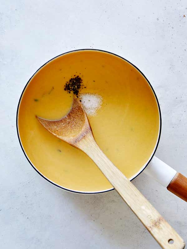 The sauce for pumpkin mac and cheese in a saucepan being seasoned with salt and pepper.