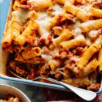 Baked ziti with some scooped out into a bowl next to it.