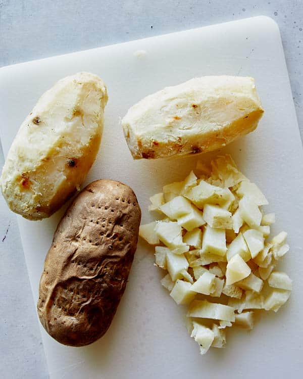 Baked potatoes peeled and diced on a cutting board.